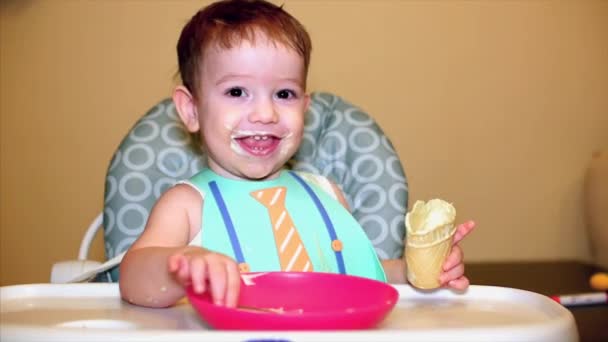 Il bambino nel pettorale mangia il gelato in una tazza di waffle, il viso del bambino viene spalmato di gelato. Bambino affascinante e mangiare gelato . — Video Stock