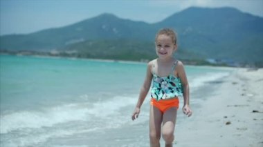 Gülümseyerek, kameraya bakarak plaj boyunca çalışan güzel küçük bir çocuk. Stok görüntüleri.