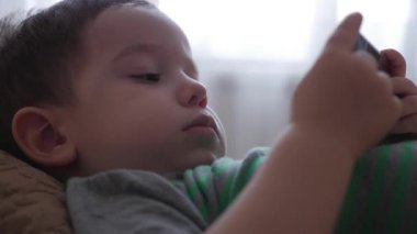 Tablet bilgisayarınızla oynarken onun kanepede yatan telefonda oynamak sevimli küçük çocuk.