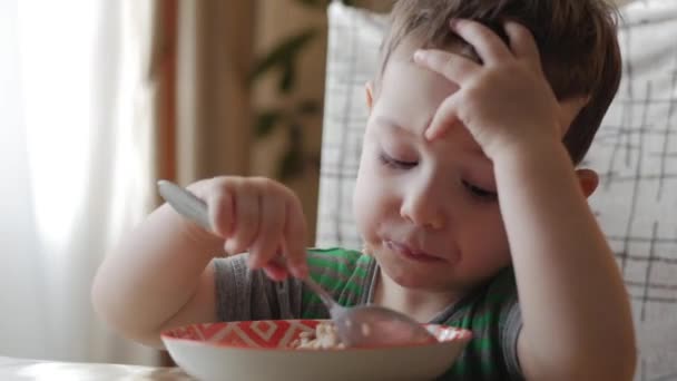 Bebé pequeno bonito sozinho come mingau de cereal com uma colher de um prato, o conceito de alimentação saudável. Instrução . — Vídeo de Stock