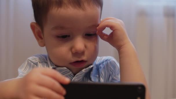 CU cara feliz del niño, un niño pequeño está acostado en el sofá del teléfono móvil, la infancia feliz . — Vídeos de Stock