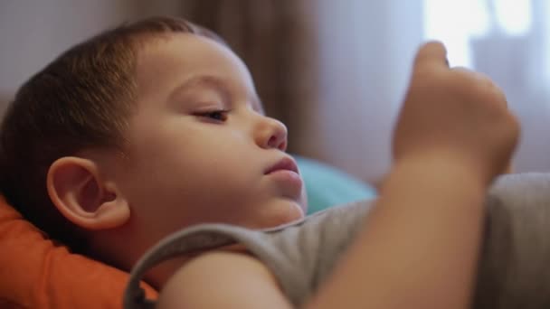 CU cara feliz del niño, un niño pequeño está acostado en el sofá del teléfono móvil, la infancia feliz . — Vídeos de Stock