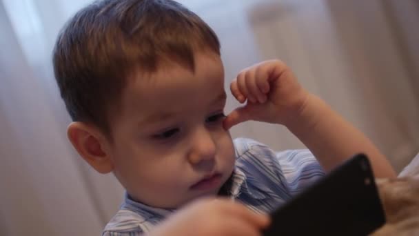 CU щасливе обличчя дитини, маленький хлопчик лежить на дивані мобільний телефон, щасливе дитинство . — стокове відео