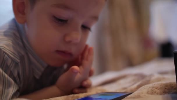 Cu χαρούμενο πρόσωπο του παιδιού, ένα μικρό αγόρι είναι ξαπλωμένος στο καναπέ κινητό τηλέφωνο, ευτυχισμένη παιδική ηλικία. — Αρχείο Βίντεο