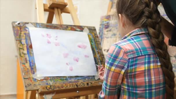 Young Pretty Artist is in the art Studio, Sitting at the Easel and Draws on Canvas, Asks the Mentor how to Draw. Drawing process: in the art Studio Girl Wth a Brush Painting on Canvas. — Stock Video