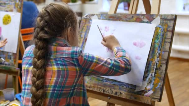 Jonge schattige artieste ligt in een Art Studio, zitten achter een ezel en schilderen op Canvas. Tekening proces: in het Art-Atelier van de kunstenaars Hand kunst meisje met een borstel schilderij op doek. — Stockvideo