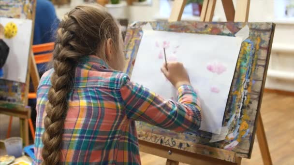 Young cute Female Artist is in an Art Studio, Sitting Behind an Easel and Painting on Canvas. Drawing Process: in the Art Studio of the Artists Hand Art Girl with a Brush Painting on Canvas. — Stock Video