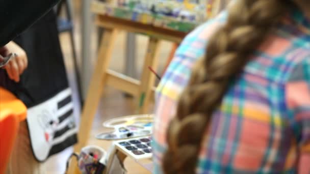 Joven artista femenina linda está en un estudio de arte, sentado detrás de un caballete y pintura sobre lienzo. Proceso de dibujo: en el estudio de arte de los artistas Hand Art Girl con un pincel Pintura sobre lienzo . — Vídeos de Stock