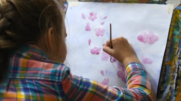 Jeune artiste féminine mignonne est dans un studio d'art, assis derrière un chevalet et peinture sur toile. Processus de dessin : dans le studio d'art des artistes Hand Art Girl avec une peinture à la brosse sur toile . — Video