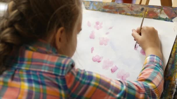 Jovem artista feminina bonito está em um estúdio de arte, sentado atrás de um cavalete e pintura na tela. Processo de Desenho: no Estúdio de Arte dos Artistas Mão Arte Menina com Pincel Pintura sobre Tela . — Vídeo de Stock