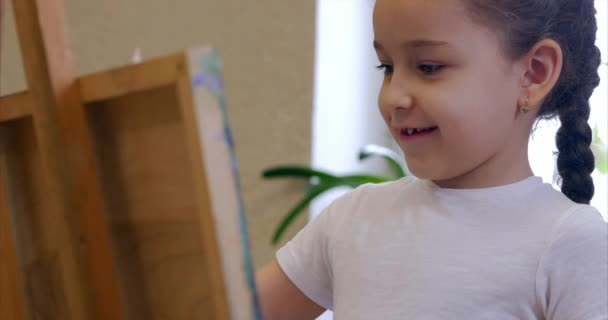 Unga händer av konstnären, lite kvinnlig konstnär målar en duk med borste, sitter en tabell och rita på duk. Processen för ritning: i konstnärer Art Studio Hand flicka skissa på Canvas.Shot närbild — Stockvideo