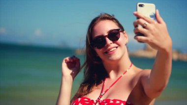 Yaz aylarında sahilde ayakta genç güzel esmer kadın, onun telefon bakıyor ve parlak gün ışığında Vietnam, arka plan mavi gökyüzü ve mavi deniz, selfie 'Ler Takes.