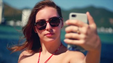 Yaz aylarında sahilde ayakta genç güzel esmer kadın, onun telefon bakıyor ve parlak gün ışığında Vietnam, arka plan mavi gökyüzü ve mavi deniz, selfie 'Ler Takes.