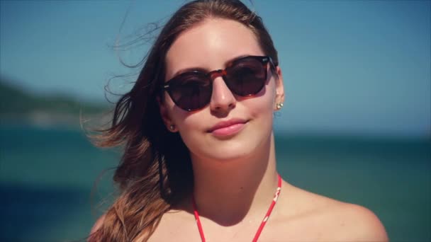 Na tropikalnej plaży Close-up portret Europejskiej piękne Śliczne Brunette w z Sunglass młoda kobieta lub wesoła dziewczyna patrząc w aparacie, dmuchanie wiatr włosy wiatr, Slow Motion. — Wideo stockowe