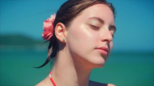 En una playa tropical Primer plano Retrato de europea hermosa linda morena con gafas de sol mujer joven o alegre chica mirando en la cámara, soplando viento pelo el viento, cámara lenta . — Vídeos de Stock