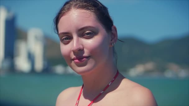 En una playa tropical Primer plano Retrato de europea hermosa linda morena con gafas de sol mujer joven o alegre chica mirando en la cámara, soplando viento pelo el viento, cámara lenta . — Vídeos de Stock