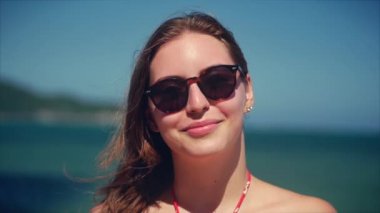 Güneş gözlüğü genç kadın veya neşeli kız kamera bakıyor ile Avrupa güzel sevimli esmer bir tropikal Plaj yakın çekim portre, Rüzgar saç rüzgar, yavaş hareket üfleme.