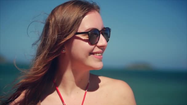 De cerca Retrato de europea hermosa linda morena joven o alegre chica sonriendo mirando a la cámara, corriendo de la mano a través del pelo soplando en el viento en la playa tropical, cámara lenta . — Vídeo de stock