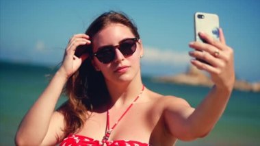 Yaz aylarında sahilde ayakta genç güzel esmer kadın, onun telefon bakıyor ve parlak gün ışığında Vietnam, arka plan mavi gökyüzü ve mavi deniz, selfie 'Ler Takes.