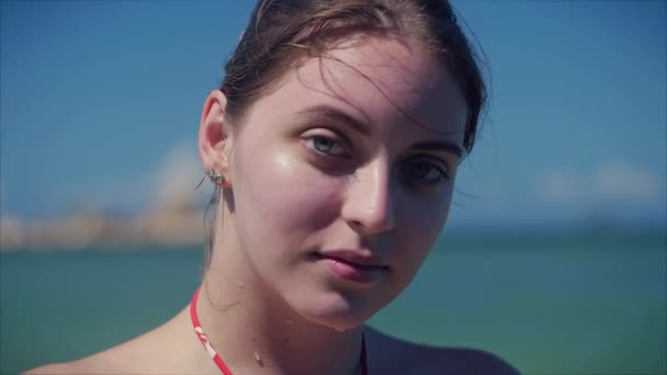 En una playa tropical Primer plano Retrato de europea hermosa linda morena con gafas de sol mujer joven o alegre chica mirando en la cámara, soplando viento pelo el viento, cámara lenta . — Vídeos de Stock