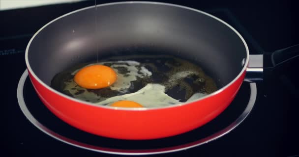 Der Koch bereitet Spiegeleier zu, kocht sie in Butter, würzt sie mit Salz, schwarzem Pfeffer und grünen Zwiebeln in einer kleinen roten Pfanne. Konzept der gesunden Ernährung. — Stockvideo