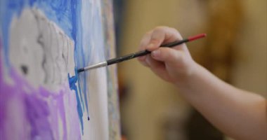 Sanatçının genç elleri, küçük kadın sanatçı fırça ile bir tuval boyar, bir masa oturan ve tuval üzerine çizin. Çizim süreci: sanatçılar sanat stüdyosu el bebek kız Canvas. Shot üzerinde çizim