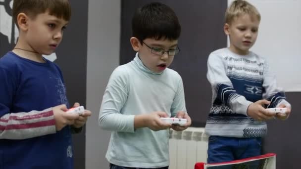 W turnieju Childrens, trzy cute dzieci grać High-Tech gry, kontrolowanie robotów z joysticki gry, zbliżenie dzieci ręce. Dzieci gry wideo. 4K — Wideo stockowe