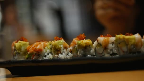 Mujer joven mano con palos toma sushi. Concepto de los rollos de sushi de los palos chinos en una placa oscura . — Vídeos de Stock