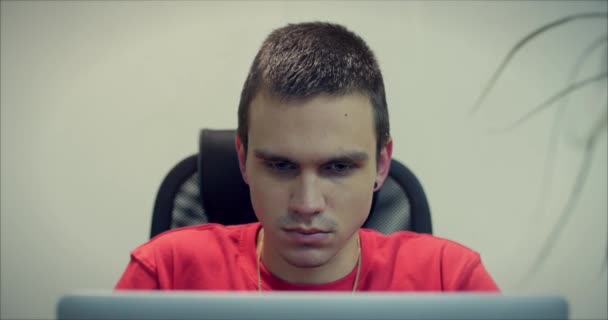 Porträt eines jungen Mannes, Programmierers oder Händlers, der mit ernstem, nachdenklichem Gesicht im Büro sitzt und an einem Laptop arbeitet. Nahaufnahme. 4k — Stockvideo