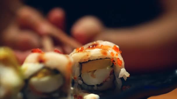 Händer liten flicka med pinnar tar sushi. Begreppet kinesiska pinnar sushi rullar på en mörk tallrik. — Stockvideo