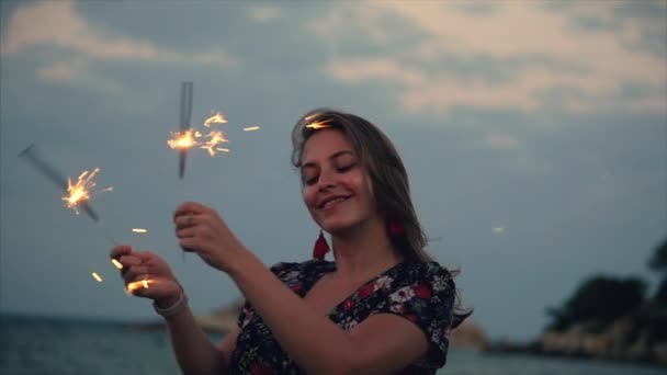 Молодая счастливая улыбающаяся женщина, танцующая с искрой на закате в замедленной съемке, с фейерверком на закате на пляже . — стоковое видео
