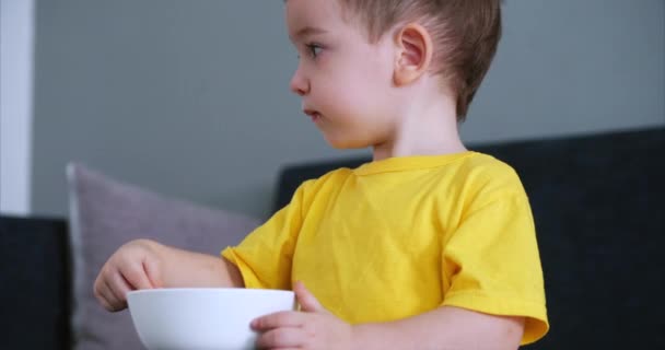 Criança pequena bonito está sentado em uma mesa e comer sua própria aveia, o bebê come de bom grado. Conceito Infância feliz . — Vídeo de Stock