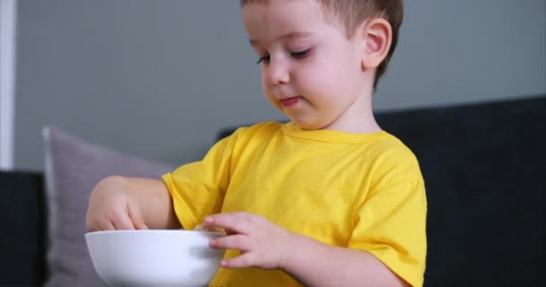 Kleines süßes Kind sitzt an einem Tisch und isst seine eigene Hafermahlzeit, das Baby isst bereitwillig. Konzept glückliche Kindheit. — Stockvideo