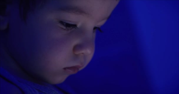 Söt barn underhåll ande med Tablet. Little Boy spendera fritid spela mobil spel i mörkret innan du går till sängs och krossar den ljusa skärmen med sin hand. Koncept teknik, barn spel — Stockvideo