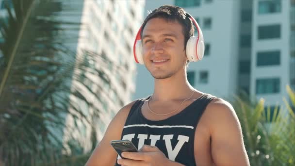 Handsome Young Man Listening Music from his Smartphone in Wireless White Headphones, Dancing on Beach Urban at Background Blue Sky. — Stok Video