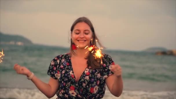 Unga glada leende kvinna, Dans in med tomtebloss i solnedgången i slow motion, med fyrverkerier vid solnedgången på stranden. — Stockvideo