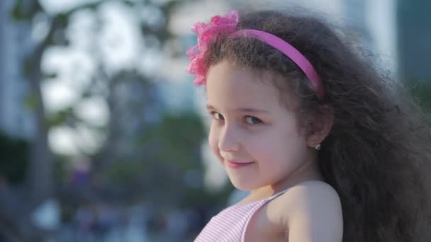Ιδέα καλή παιδική ηλικία. Πορτρέτο χαριτωμένο μικρό παιδί Καυκάσιος θηλυκό, παιδί σε εξωτερικούς χώρους σε ένα ροζ φόρεμα με ένα ροζ λουλούδι στο κεφάλι της, κοιτάζοντας στην κάμερα. Ιδέα καλή παιδική ηλικία. — Αρχείο Βίντεο