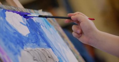 Sanatçının genç elleri, küçük kadın sanatçı fırça ile bir tuval boyar, bir masa oturan ve tuval üzerine çizin. Çizim süreci: sanatçılar sanat stüdyosu el bebek kız Canvas. Shot üzerinde çizim