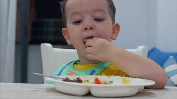 Śliczne małe dziecko siedzi przy stole na szelkach i jeść własne puree, Baby zjada chętnie. Koncepcja Happy Childhool. — Wideo stockowe