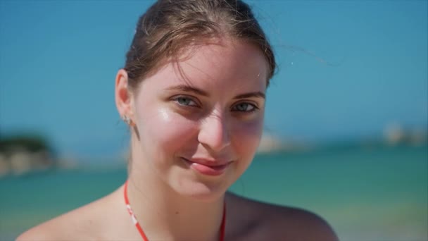 Op een tropisch strand close-up portret van Europese mooie schattige brunette in met een zonnebril jonge vrouw of vrolijk meisje op zoek in de camera, waait wind haar de wind, Slow Motion. — Stockvideo