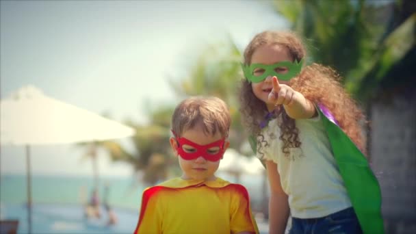 Los niños vestidos con disfraces de superhéroes, capas y máscaras juegan a los héroes y se divierten en el Glade de verano en el parque. Concepto de una Infancia Feliz . — Vídeo de stock