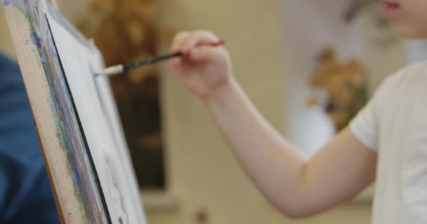 Unga händer av konstnären, liten kvinna konstnär målar en canvas med pensel, sittande ett bord och rita på canvas. Process för ritning: i Artists Art Studio hand Baby Girl skissa på canvas. shot CloseUp — Stockvideo