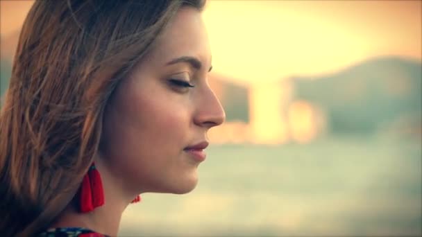 Close up Retrato uma mulher de cabelos castanhos maravilhoso com olhos verdes com fluxo de cabelo em um vestido de verão com uma imagem de flores vermelhas e brancas contra a árvore verde no Set Sun. Foco suave — Vídeo de Stock