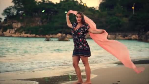 Fermer Portrait Une merveilleuse femme aux cheveux bruns aux yeux verts avec des cheveux fluides dans une robe d'été avec une image de fleurs rouges et blanches contre l'arbre vert au coucher du soleil. Focus doux — Video