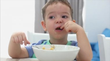 Küçük sevimli çocuk bir masada oturuyor ve kendi yulaf ezmesi yemek, Bebek isteyerek yiyor. Konsept mutlu çocukluk.