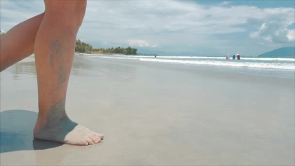 На тропічному пляжі крупним планом жіночий ноги європейських Cute брюнетка йде під спекотним літнім сонцем уздовж тропічного екзотичного узбережжя, безтурботна дівчина ходить по піску право на океан, повільний рух. — стокове відео