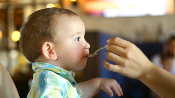 母がレストランで赤ちゃんスプーンから離乳食を与える、子供が喜んで食べる。4 k. — ストック動画