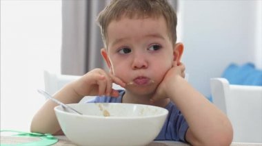 Küçük sevimli çocuk bir masada oturuyor ve kendi yulaf ezmesi yemek, Bebek isteyerek yiyor. Konsept mutlu çocukluk.