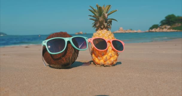 Em uma praia tropical Close-Up de frutas em óculos de sol sob o sol quente de verão ao longo da costa tropical exótica, abacaxi e coco em óculos de sol no fundo do Oceano.Conceito Verão, Festa, Feriado — Vídeo de Stock