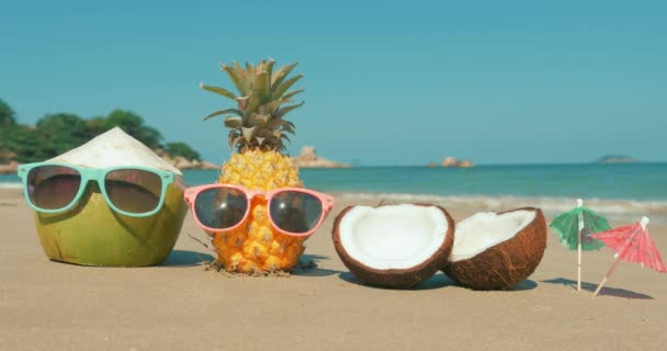 Em uma praia tropical Close-Up de frutas em óculos de sol sob o sol quente de verão ao longo da costa tropical exótica, abacaxi e coco em óculos de sol no fundo do Oceano.Conceito Verão, Festa, Feriado — Vídeo de Stock